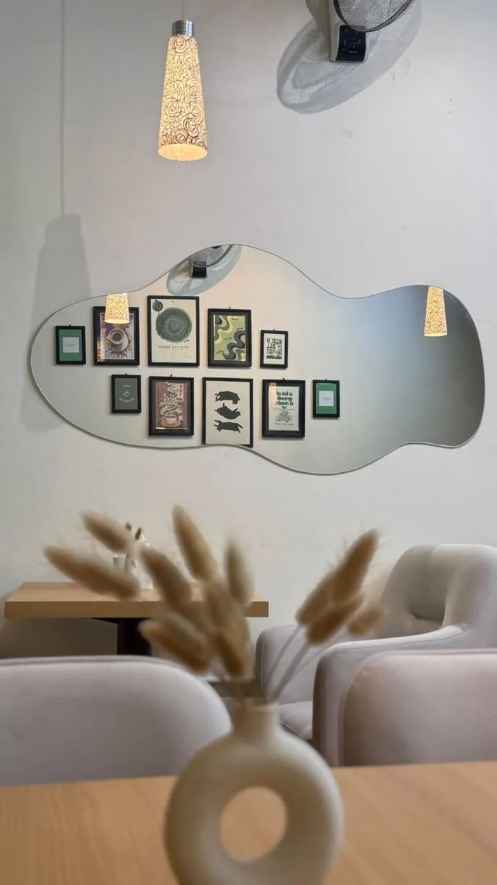 A cloud-shaped mirror reflecting framed prints, with pampas grass in the foreground